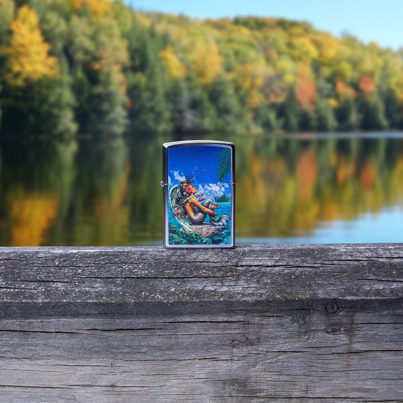 Lifestyle image of Rick Rietveld Mermaid Design Street Chrome?äó Windproof Lighter standing on a railing outside, with trees and water in the background.