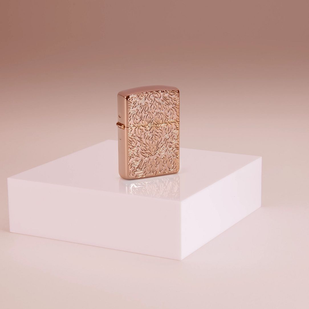Lifestyle image of Zippo Carved Armor?« Rose Gold Design Windproof Lighter standing on a riser in a pink background.